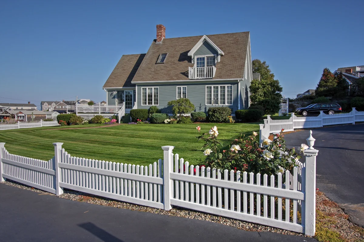 Beautiful landscaped home with manicured lawn and white picket fence